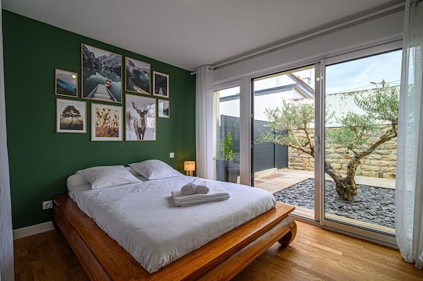 Une chambre avec un grand lit, une vue sur l’extérieur et plusieurs tableaux encadrés accrochés au mur.