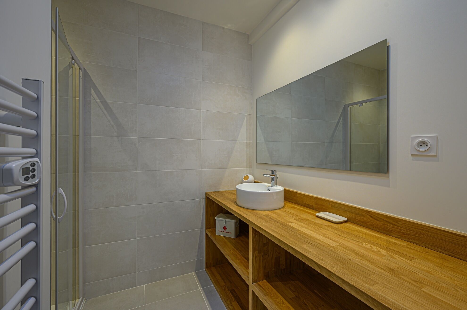 Une salle de bain avec une douche à parois de verre, un lavabo blanc, un meuble-lavabo en bois et un grand miroir.