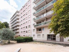 Un immeuble résidentiel à plusieurs étages, doté de balcons, d’une zone pavée et d’un arbre.