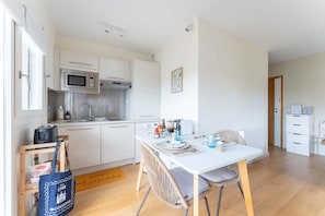 Une cuisine moderne avec des meubles blancs, un four à micro-ondes et un évier. On y trouve une table à manger avec des chaises et un petit tapis.