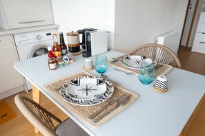 Une table à manger dressée avec des assiettes, des verres et des couverts, avec une machine à café et des bouteilles en arrière-plan.