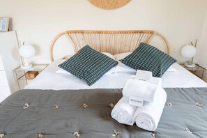 A neatly made bed with a grey bedspread, two green pillows, and a white towel.