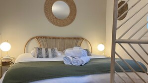 A neatly made bed with rolled towels, a woven headboard, and a round mirror on the wall. - LE NID DES CEDRES - Magnifique Studio terrasse Montplaisir (Lyon)
