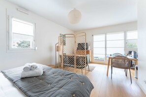 Een slaapkamer met een bed, een bureau, een stoel, een raam en een balkon.
