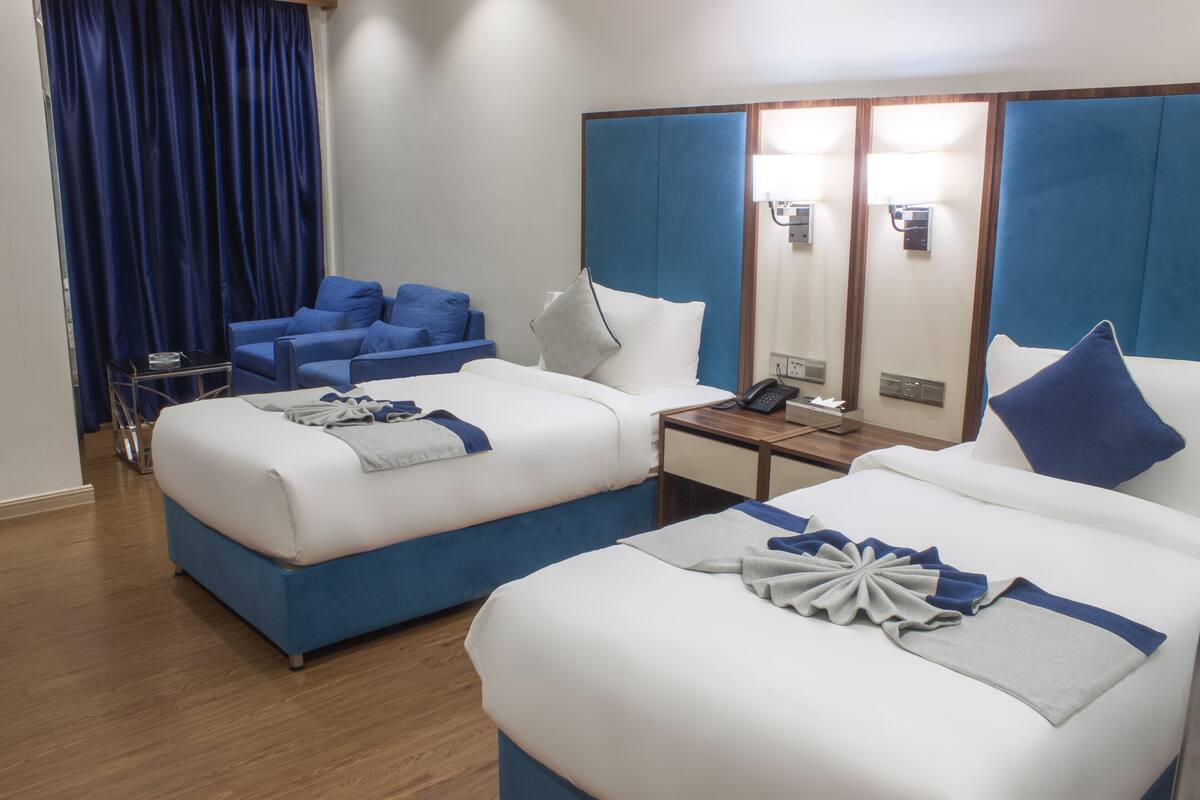 A hotel room with two beds, a desk, a chair, a mirror, and a blue curtain.