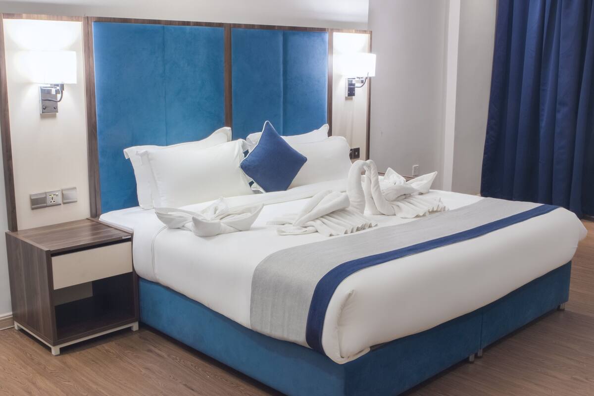 A hotel room with a large bed, a nightstand, and a mirror.