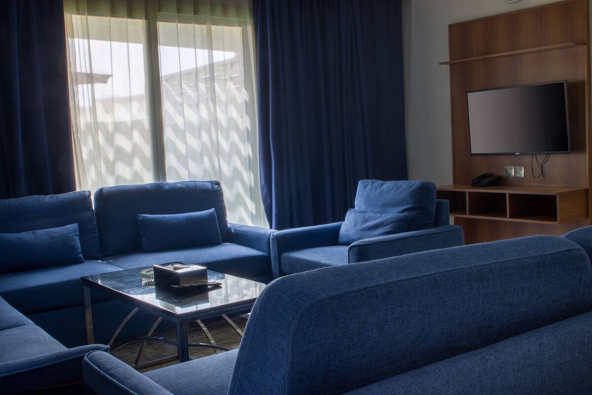 A modern living room with a sectional sofa, a coffee table, and a flat-screen TV mounted on a wooden wall.