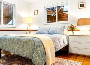 Un dormitorio con cama, mesitas de noche, lámpara, ventana y vistas a una escalera de madera.