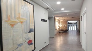 A hotel corridor with a large painting of martini glasses and a bottle, a sign reading "ASEOS," and a dining area in the distance. - Micampus Burgos Centro (Burgos)
