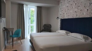 A hotel room with a large bed, a desk with a chair, and a window with curtains. - Micampus Burgos Centro (Burgos)
