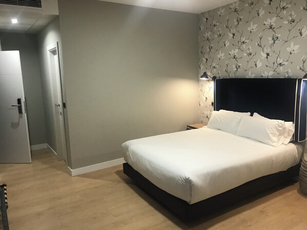 A bedroom with a bed, a nightstand, a lamp, and a door.