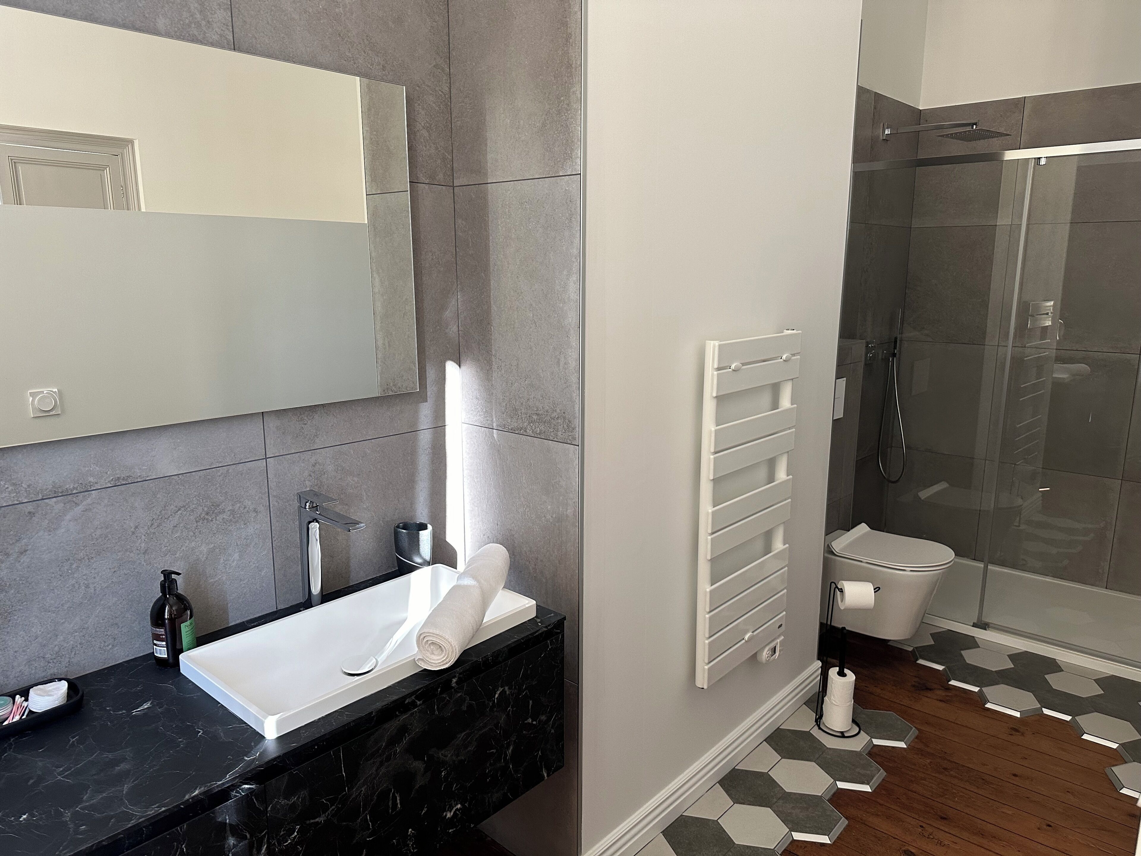 A modern bathroom with a black marble countertop, a white sink, a large mirror, a towel, a shower with a glass door, and a toilet.