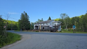 A two-story building with a porch and a staircase leading to the upper floor. - Country Lodge for Large Groups & Families | All-Inclusive Available (Sainte-Marguerite-du-Lac-Masson)