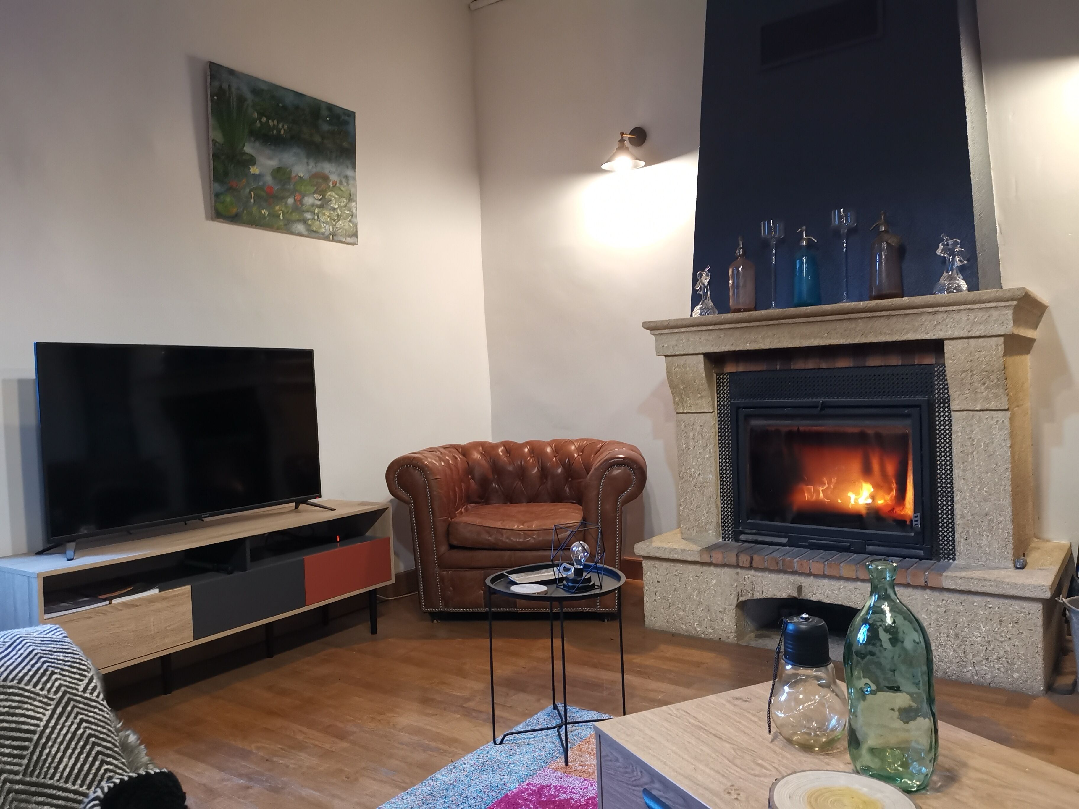 Un salon avec un canapé en cuir, un téléviseur à écran plat, une cheminée et un tableau accroché au mur.