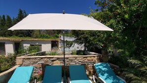 Eine Terrasse mit vier Liegestühlen, einem weißen Sonnenschirm und einer Steinmauer.