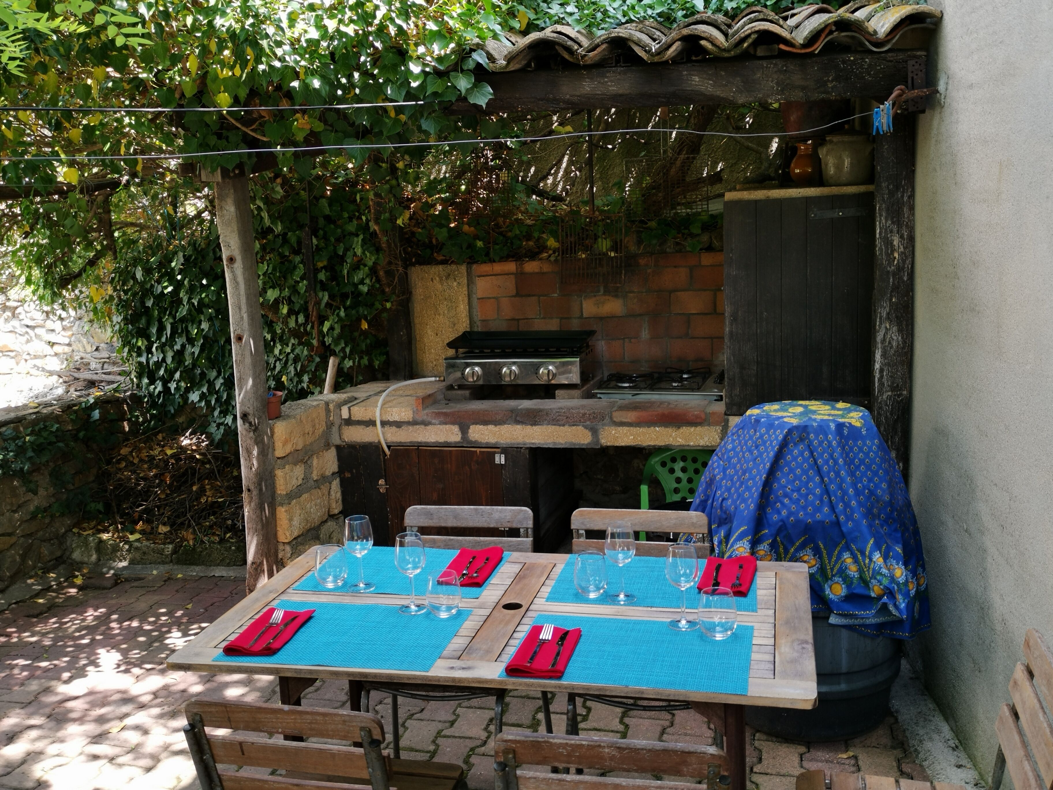 Un espace extérieur aménagé pour les repas, avec un barbecue en briques, des tables et des chaises en bois.