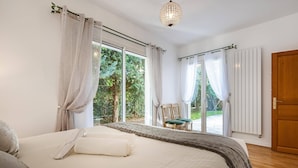 Ein Schlafzimmer mit einem großen Bett, Blick ins Grüne durch die Fenster und einer Holztür.