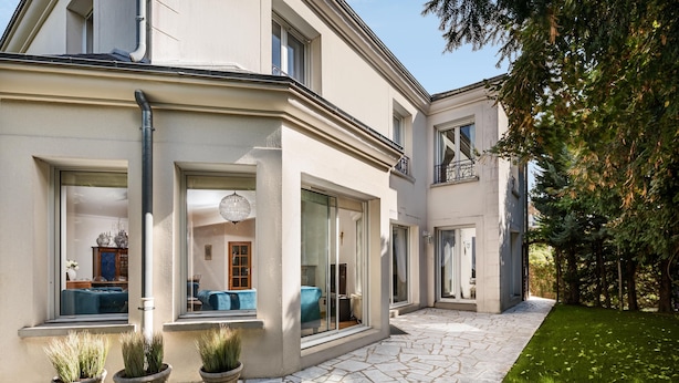 Ein modernes Haus mit Steinterrasse, großen Fenstern und einem gepflegten Rasen.