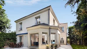 Ein zweistöckiges Haus mit überdachter Terrasse, großen Fenstern und einem gepflegten Rasen.
