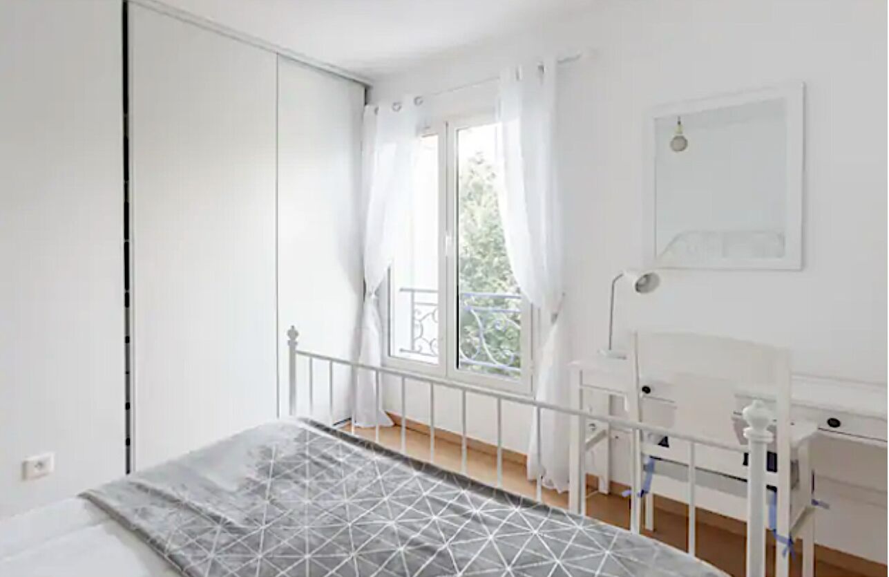 Un dormitori amb un llit, una finestra amb cortines, un escriptori blanc i una cadira blanca.
