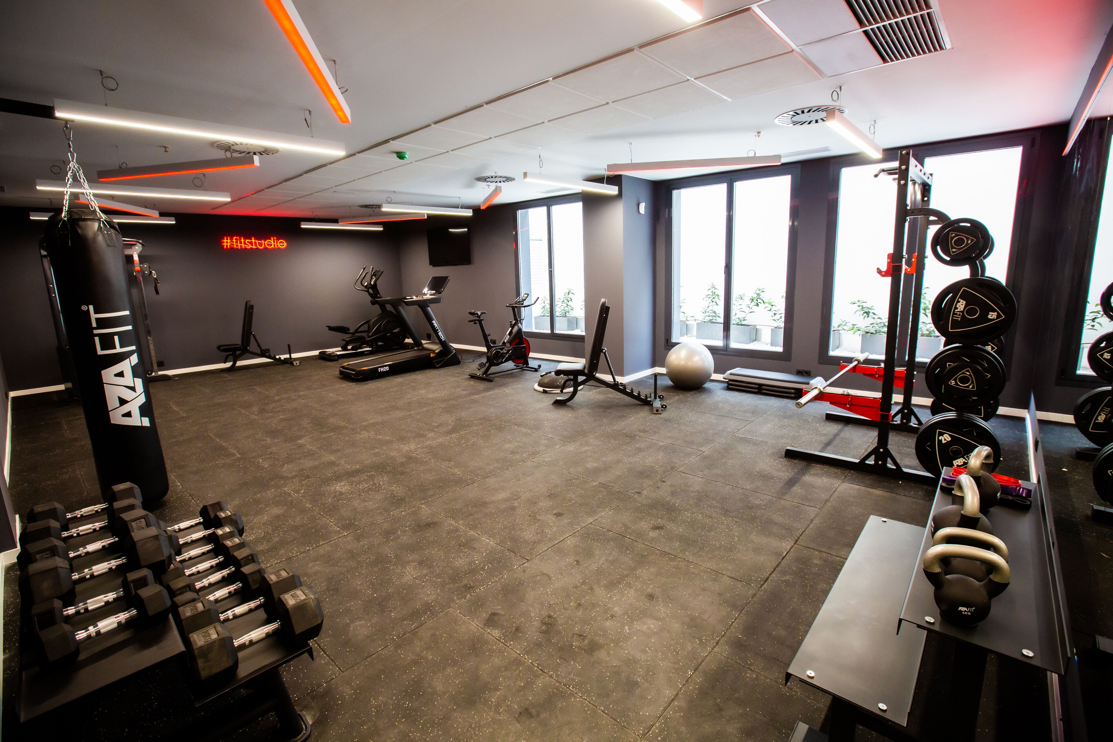Un gimnasio con diversos equipos de ejercicio, incluyendo mancuernas, kettlebells y un saco de boxeo.