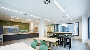 A modern coffee shop with a glass display case, green chairs, and a wooden table. - Micampus Residencia Estudiantes Burjassot Parque (Burjasot)