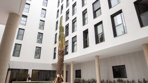 A modern building with a central courtyard, featuring a tall palm tree, green planters, and a seating area. - Micampus Residencia Estudiantes Burjassot Parque (Burjasot)