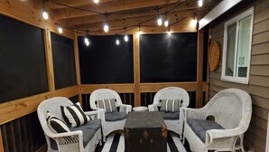 Une terrasse couverte avec des meubles en osier, un tapis rayé noir et blanc et des guirlandes lumineuses.