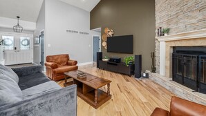 Un vaste salon doté d’une cheminée en pierre, d’un grand téléviseur à écran plat fixé au mur et d’un fauteuil en cuir.