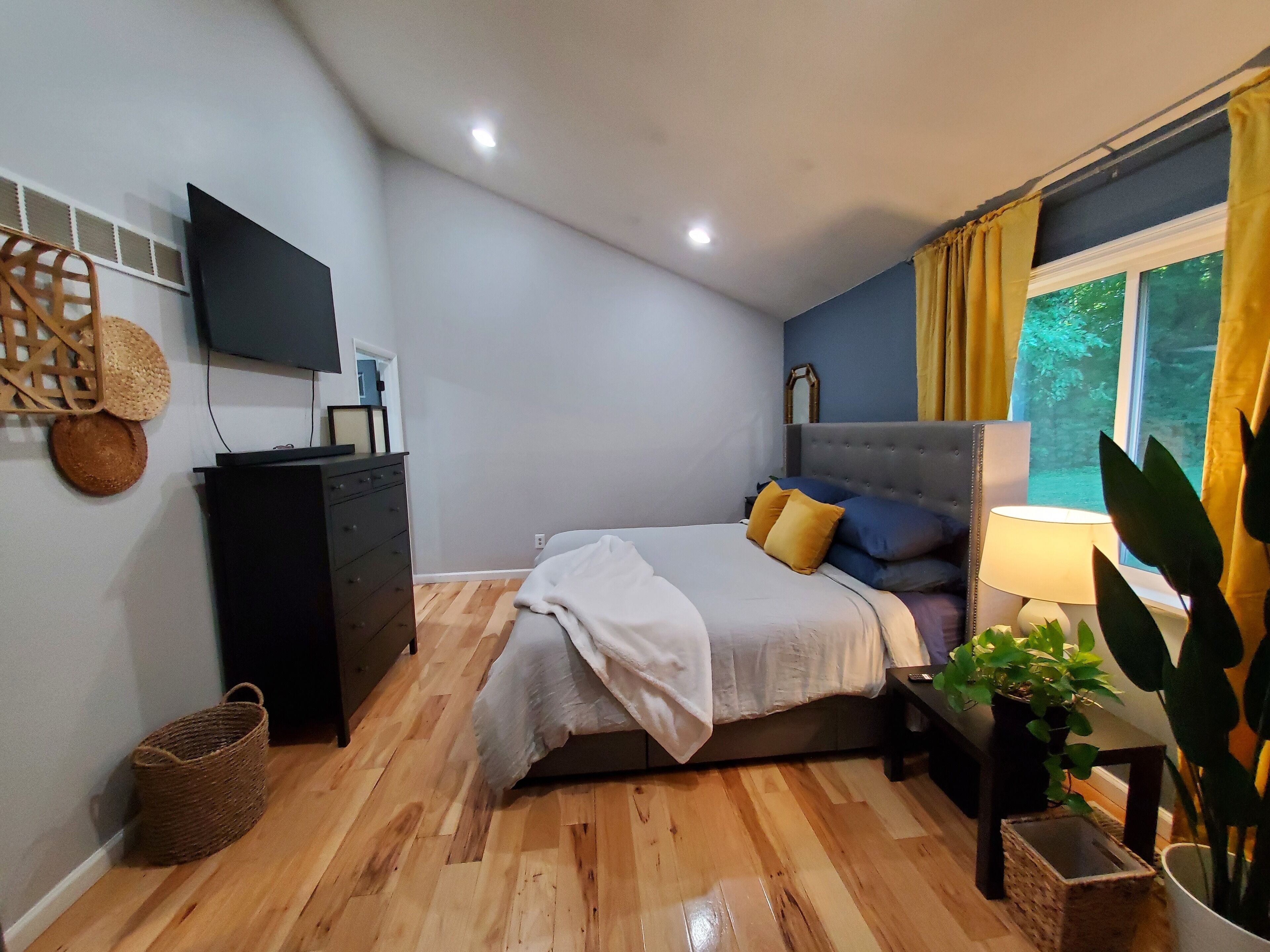 A bedroom with a bed, a dresser, a TV, and a window with curtains.