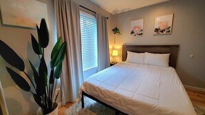 Une chambre d’hôtel avec un lit, une table de chevet, une lampe, une plante et des œuvres d’art accrochées aux murs.
