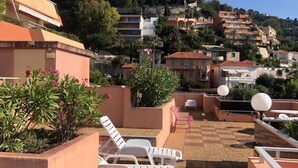 Una terraza en la azotea con sillones blancos, una mesita y plantas en macetas.