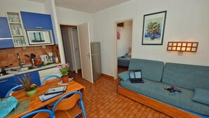Un espacio habitable compacto con kitchenette, una zona de comedor con mesa y sillas, un sofá y una obra de arte enmarcada en la pared.