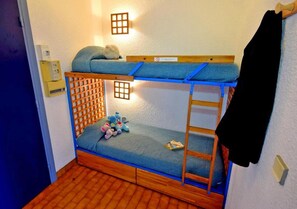 A bunk bed with a wooden frame, a blue mattress, and a ladder. There are toys on the bed and a black jacket hanging on the wall.
