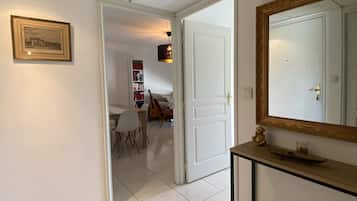 A hallway with a tiled floor, a framed picture on the wall, a white door, and a console table with a mirror and a small shelf.