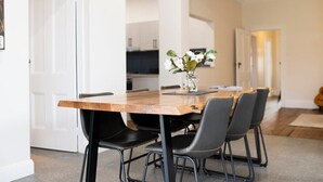 A dining area with a wooden table and black chairs, a vase with flowers, and a kitchen in the background. - Best Nest on March. Firepit Cottage. Walk to CBD. (Orange)