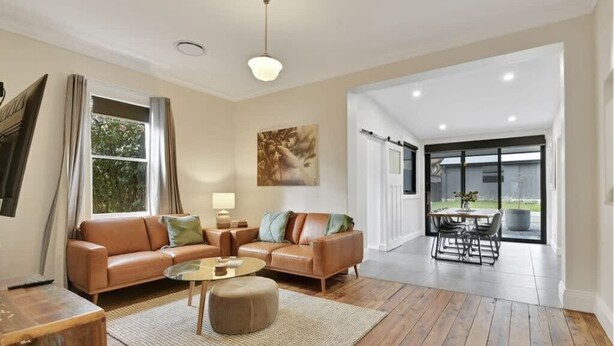 A spacious living room with a leather sofa, round coffee table, and a dining area with a table and chairs. - Best Nest on March. Firepit Cottage. Walk to CBD. (Orange)