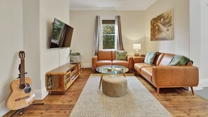 A living room with a sofa, ottoman, and a glass coffee table. - Best Nest on March. Firepit Cottage. Walk to CBD. (Orange)