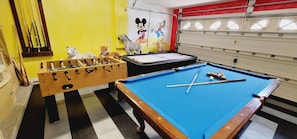 Une table de billard recouverte d’un drap bleu, une table de baby-foot et une fresque murale représentant des personnages de dessins animés.