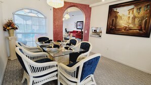Zona pranzo con tavolo in vetro, sedie in vimini e un divano rosso sullo sfondo.