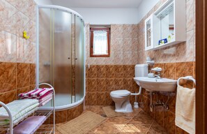 Une salle de bain avec une douche, des toilettes, un lavabo et une petite fenêtre.