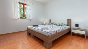 Ein Schlafzimmer mit einem hölzernen Bett, einem Nachttisch, einem Fenster mit Vorhängen und einer Pflanze.