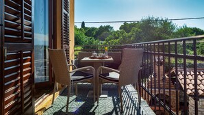 Eine Terrasse im Freien mit Korbmöbeln, einem Tisch mit einer Vase und Blick auf Grünflächen und Gebäude im Hintergrund.