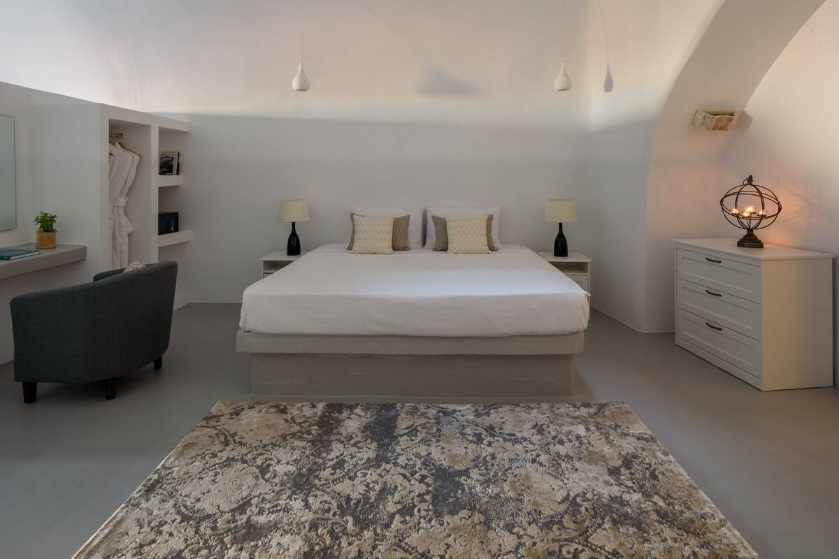 A bedroom with a skylight, a bed with multiple pillows, bedside tables, a nightstand, a desk, and a chair.