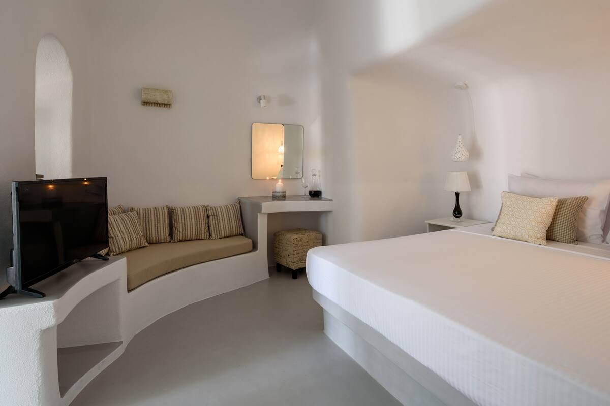 A modern hotel room with a sofa, a bed, a TV, a mirror, and a lamp.