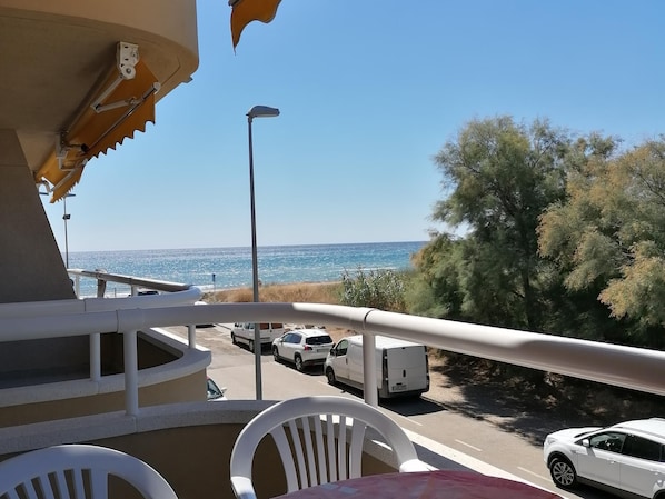 A balcony with a view of the sea, a street with parked cars, and a white car in the foreground. - Apartment 2/4 sea view (L'Estartit)