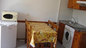 A compact kitchen with a microwave, washing machine, sink, and a table with a fruit-patterned tablecloth. - Apartment 2/4 sea view (L'Estartit)