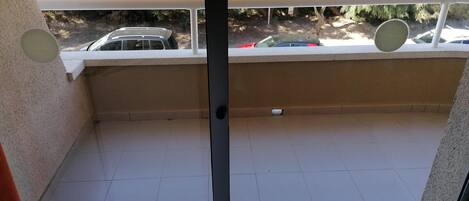 A balcony with a tiled floor, a white railing, and a view of parked cars and trees.