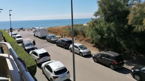 Un espace de stationnement où sont garées plusieurs voitures et une caravane, avec vue sur une plage sous un ciel dégagé.