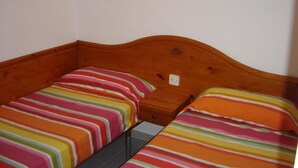 Une petite chambre avec deux lits simples, chacun recouvert d’une courtepointe rayée aux couleurs vives.